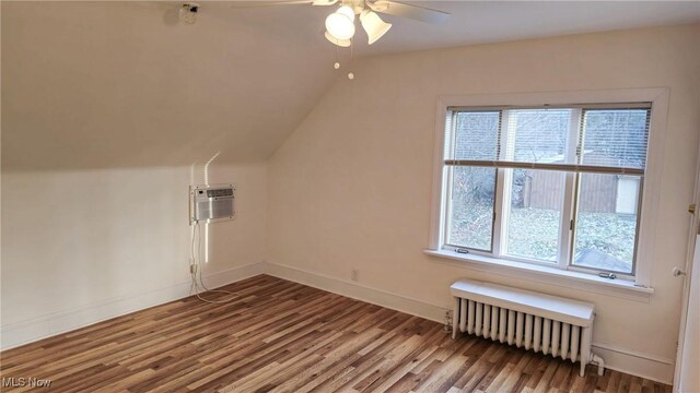 bonus room featuring radiator, vaulted ceiling, a wall unit AC, ceiling fan, and hardwood / wood-style floors