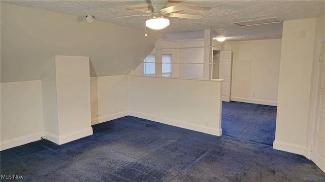 additional living space with ceiling fan, dark carpet, and a textured ceiling