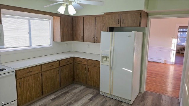 kitchen with ceiling fan, white fridge with ice dispenser, a baseboard radiator, stove, and hardwood / wood-style flooring