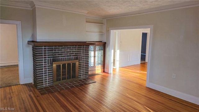 unfurnished living room with built in features, a baseboard heating unit, crown molding, wood-type flooring, and a tiled fireplace