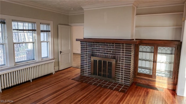 unfurnished living room featuring a fireplace, radiator heating unit, crown molding, and wood-type flooring