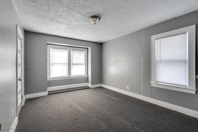 empty room with dark carpet and a textured ceiling