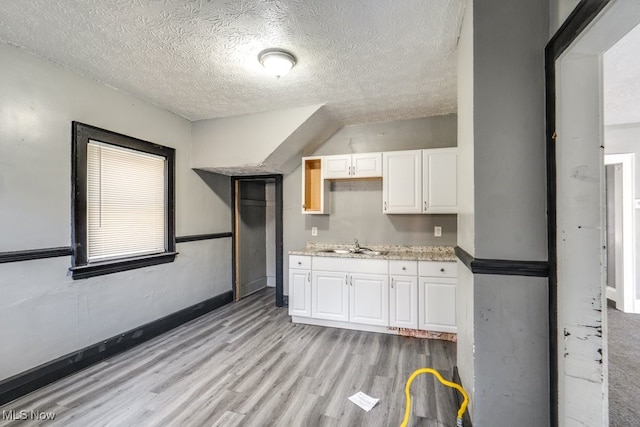 kitchen with sink, white cabinets, light hardwood / wood-style floors, and a textured ceiling