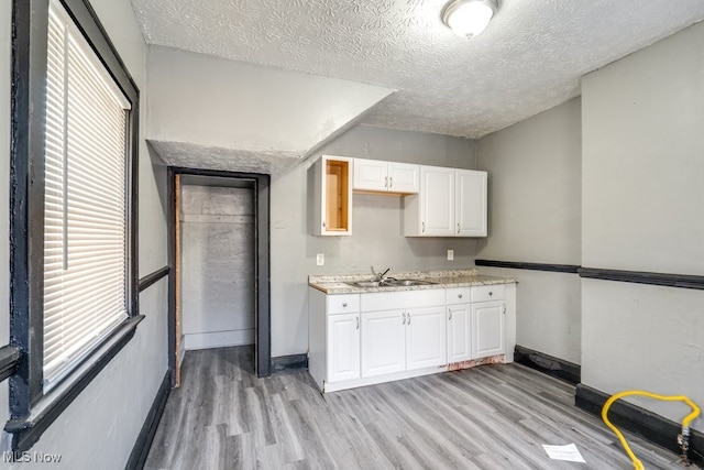 kitchen featuring white cabinets, light wood-type flooring, sink, and a textured ceiling