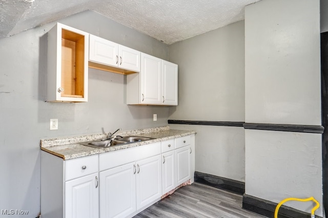 kitchen with sink, white cabinets, a textured ceiling, and light hardwood / wood-style flooring