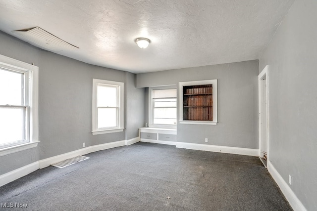 spare room featuring a textured ceiling and dark carpet