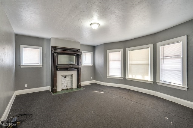 unfurnished living room with plenty of natural light, dark carpet, and a textured ceiling