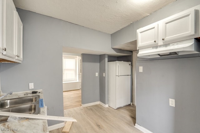 kitchen with white fridge, sink, white cabinetry, and a textured ceiling