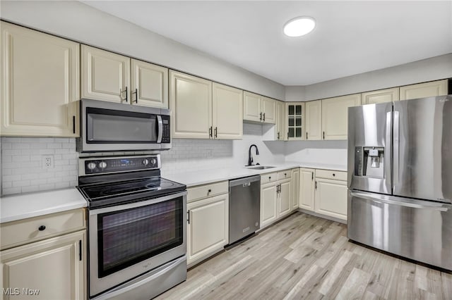 kitchen with light wood-type flooring, tasteful backsplash, stainless steel appliances, sink, and cream cabinets