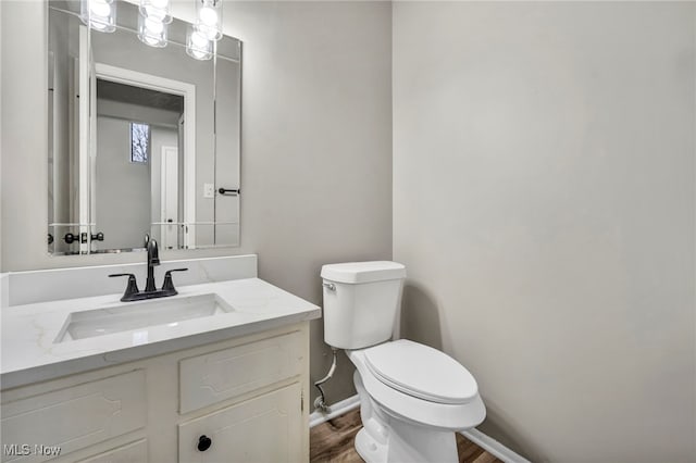 half bathroom featuring baseboards, toilet, wood finished floors, and vanity