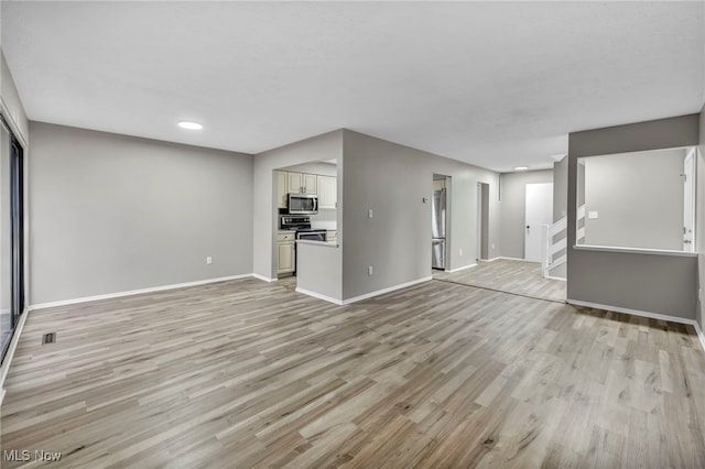 unfurnished living room featuring stairway, baseboards, visible vents, and light wood finished floors