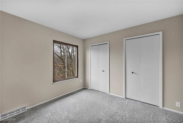 unfurnished bedroom featuring visible vents, baseboards, two closets, and carpet