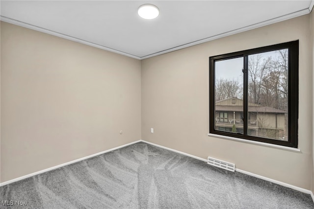 empty room featuring crown molding, carpet, visible vents, and baseboards