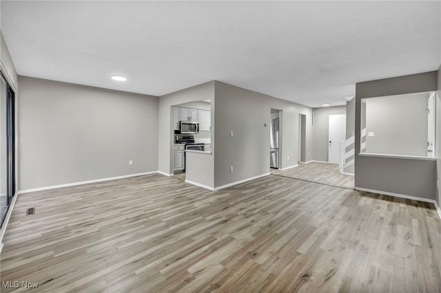 unfurnished living room featuring stairs, light wood-style flooring, visible vents, and baseboards