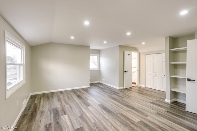 spare room with hardwood / wood-style floors, built in shelves, and lofted ceiling