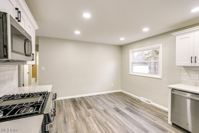 kitchen featuring decorative backsplash, white cabinetry, light wood-type flooring, and appliances with stainless steel finishes