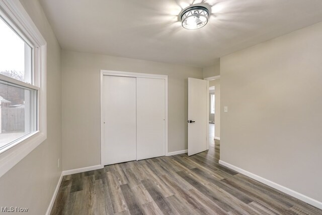 unfurnished bedroom featuring multiple windows, a closet, and dark wood-type flooring