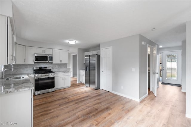 kitchen with sink, light stone counters, decorative backsplash, appliances with stainless steel finishes, and light wood-type flooring