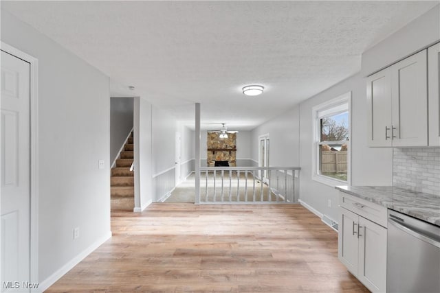 interior space with dishwasher, backsplash, a stone fireplace, light stone counters, and white cabinetry