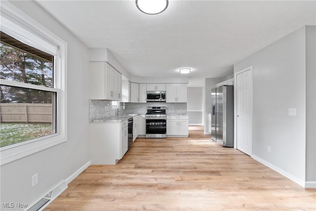 kitchen featuring a healthy amount of sunlight, decorative backsplash, white cabinetry, and stainless steel appliances