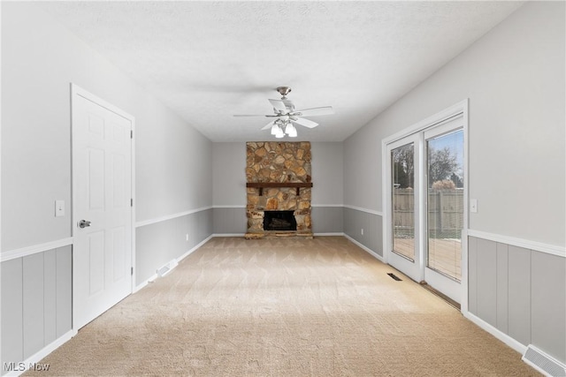 unfurnished living room with ceiling fan, a fireplace, light carpet, and a textured ceiling