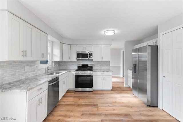 kitchen featuring decorative backsplash, appliances with stainless steel finishes, sink, white cabinets, and light hardwood / wood-style floors