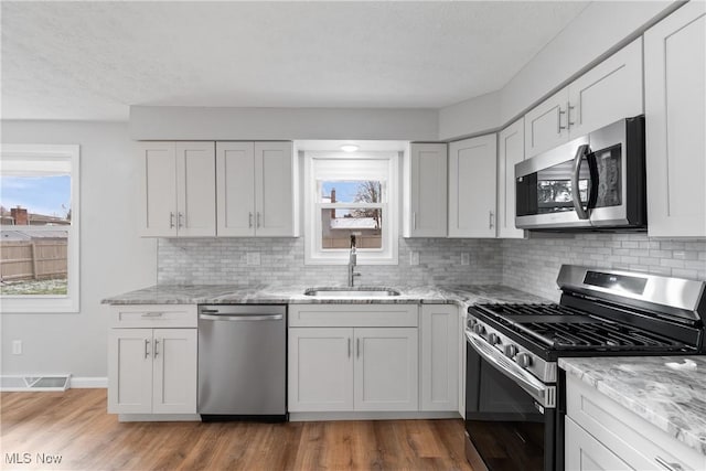 kitchen featuring decorative backsplash, appliances with stainless steel finishes, light stone counters, sink, and white cabinetry