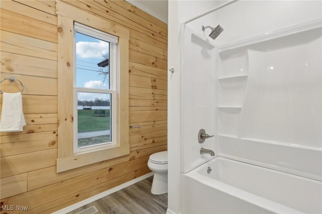 bathroom with hardwood / wood-style floors, washtub / shower combination, wooden walls, and toilet