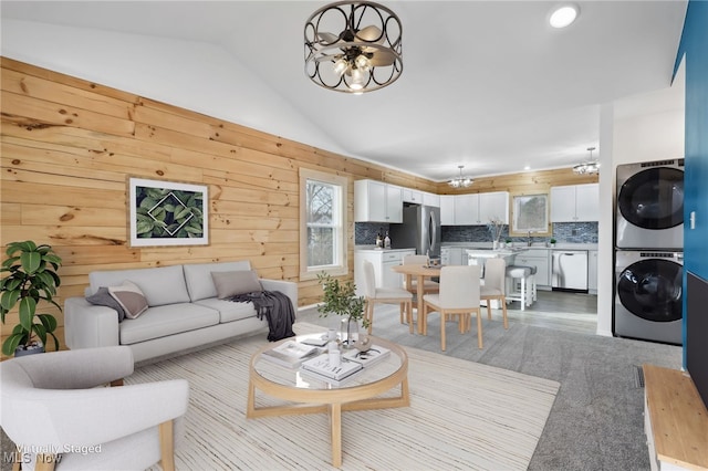 living room with stacked washer / dryer, a chandelier, and vaulted ceiling