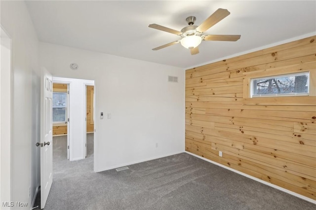 carpeted spare room featuring ceiling fan and wood walls