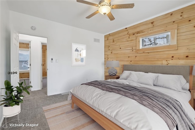 bedroom featuring multiple windows, wooden walls, light colored carpet, and ceiling fan