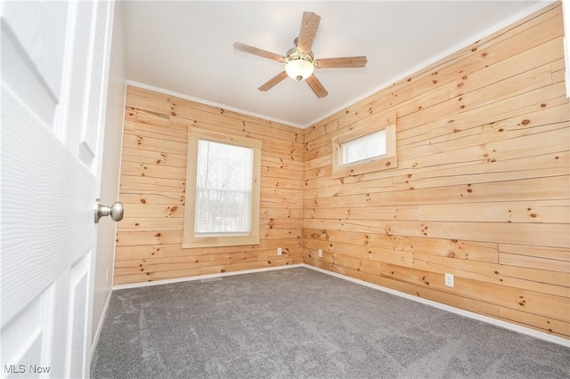 spare room with crown molding, ceiling fan, wooden walls, and dark carpet