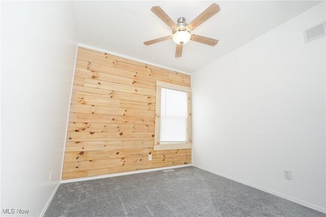 spare room with dark colored carpet, ceiling fan, and wood walls