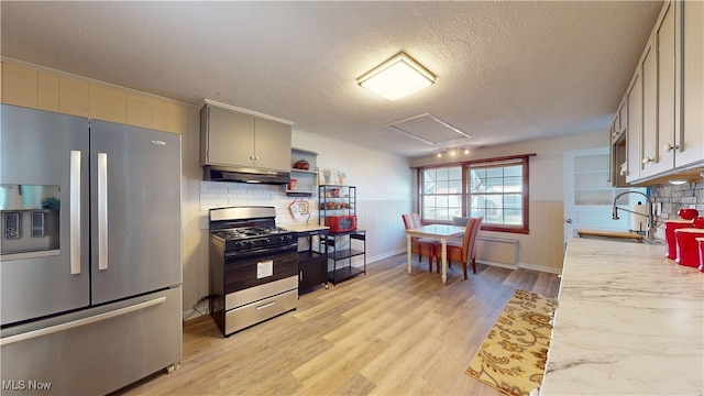 kitchen with stainless steel fridge, tasteful backsplash, gas range, sink, and light hardwood / wood-style floors