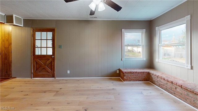 empty room with crown molding, wood walls, and light wood-type flooring
