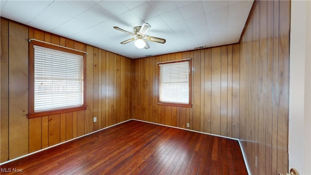 spare room with ceiling fan, wooden walls, and dark wood-type flooring