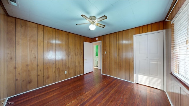 unfurnished bedroom featuring dark hardwood / wood-style floors, ceiling fan, and wood walls