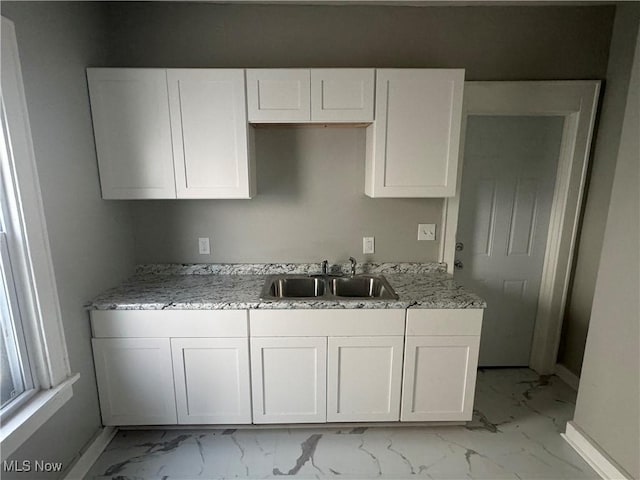 kitchen featuring white cabinets, light stone counters, and sink