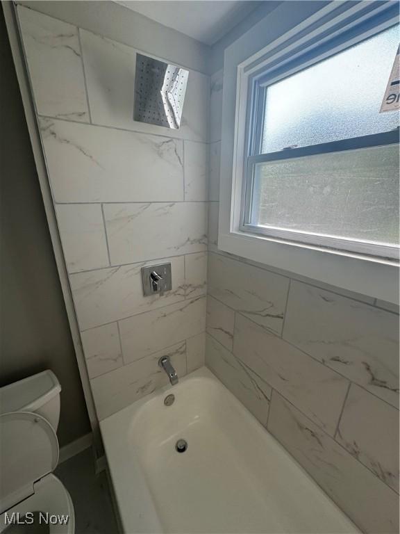 bathroom featuring tiled shower / bath combo and toilet