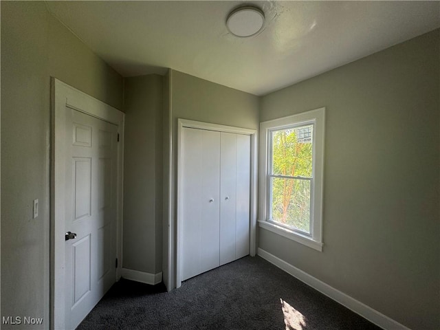 unfurnished bedroom with dark carpet and a closet