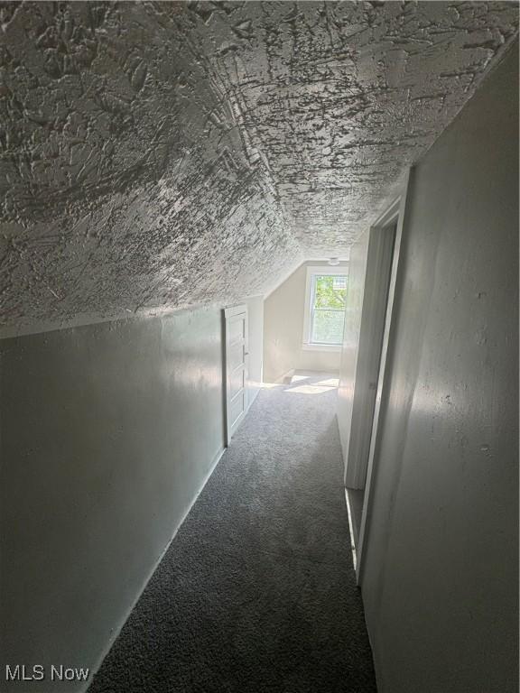 hallway featuring lofted ceiling, carpet, and a textured ceiling