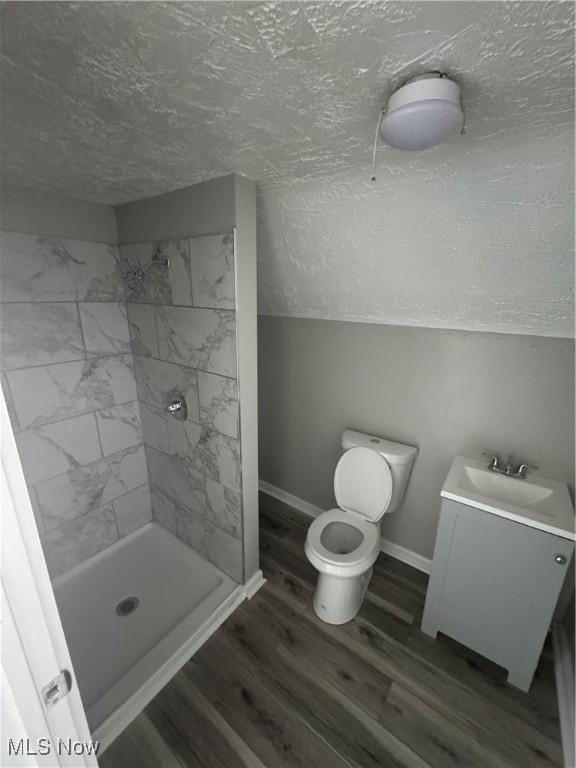 bathroom featuring hardwood / wood-style floors, vanity, toilet, tiled shower, and a textured ceiling