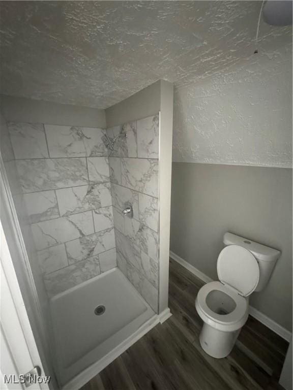 bathroom featuring a tile shower, wood-type flooring, a textured ceiling, and toilet