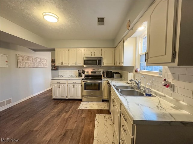 kitchen featuring decorative backsplash, a textured ceiling, stainless steel appliances, dark wood-type flooring, and sink