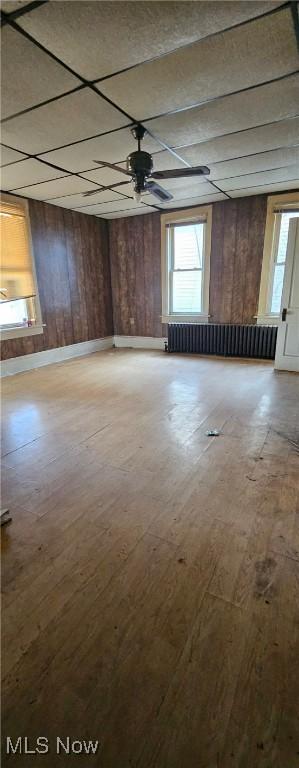 unfurnished room with wooden walls, radiator heating unit, ceiling fan, and hardwood / wood-style floors