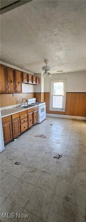 kitchen featuring ceiling fan, wood walls, sink, and white range with gas cooktop