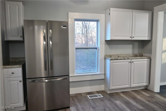 kitchen with white cabinets, dark hardwood / wood-style floors, stainless steel fridge, and light stone countertops