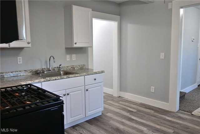 kitchen with white cabinets, light hardwood / wood-style floors, black range, and sink