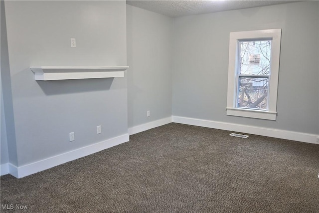 spare room featuring dark carpet and a textured ceiling