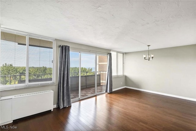 unfurnished room featuring radiator, dark wood-type flooring, a textured ceiling, and a notable chandelier